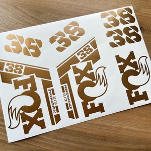 May include: A sheet of gold-coloured stickers with the words "Performance Elite" and the number "38" repeated multiple times. The stickers are designed for a bicycle.