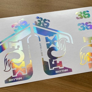 May include: A sheet of holographic stickers featuring the Fox Racing logo, the words "Rhythm" and "36", and the text "308 V1" and "Thirty Six".