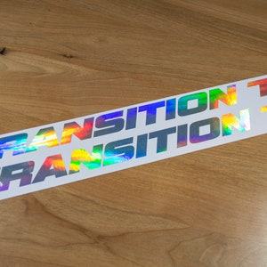 Puede incluir: Dos pegatinas iridiscentes arcoíris con el texto "TRANSITION TR" sobre un fondo blanco.
