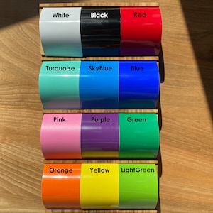 May include: A set of 10 color swatches displayed on a wooden board. The colors are white, black, red, turquoise, sky blue, blue, pink, purple, green, orange, yellow, and light green.