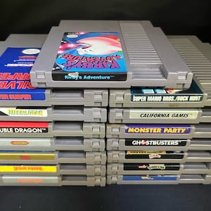 May include: A collection of retro Nintendo Entertainment System (NES) game cartridges. Titles include "Kirby's Adventure," "Silver Surfer," "Double Dragon," and "Super Mario Bros./Duck Hunt." The cartridges are grey with colourful label art.