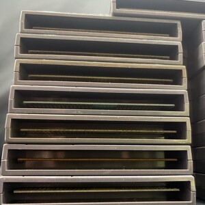 May include: A collection of grey rectangular game cartridges. Each cartridge features a rectangular opening and a gold-coloured connector. The cartridges are stacked together.