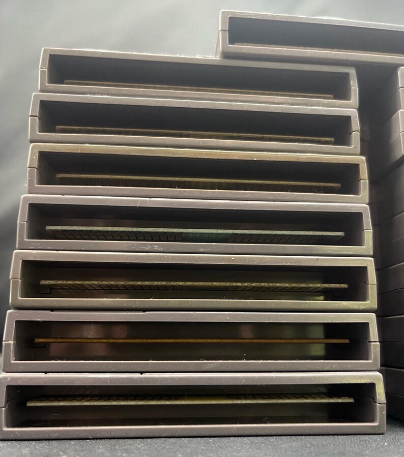 May include: A collection of grey rectangular game cartridges. Each cartridge features a rectangular opening and a gold-coloured connector. The cartridges are stacked together.