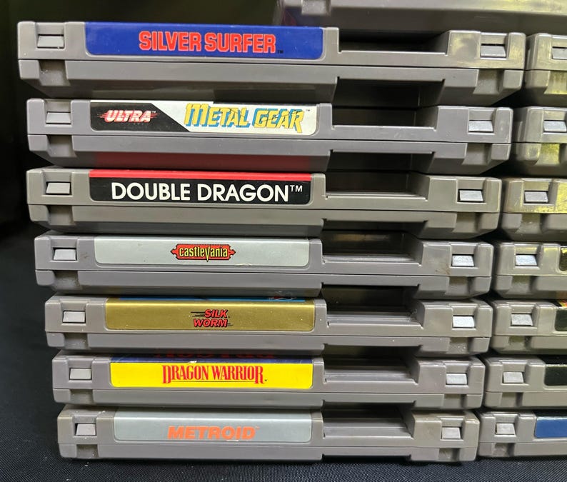 May include: A collection of retro NES game cartridges. Titles visible include "Silver Surfer," "Metal Gear," "Double Dragon," "Castlevania," "Silk Worm," "Dragon Warrior," and "Metroid." The cartridges are grey with colourful labels.