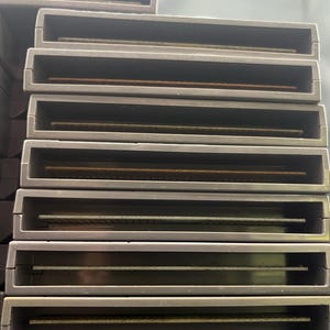 May include: A stack of grey rectangular game cartridges. Each cartridge has a recessed slot with a gold-coloured connector visible inside. The cartridges are stacked on top of each other.
