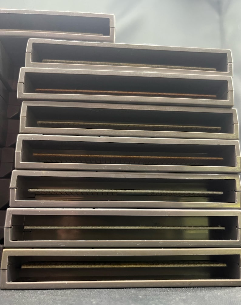 May include: A stack of grey rectangular game cartridges. Each cartridge has a recessed slot with a gold-coloured connector visible inside. The cartridges are stacked on top of each other.