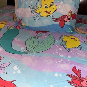 May include: A white ceramic mug with a black handle and the text "But First, Coffee" in a black, handwritten-style font. The mug is on a white surface.