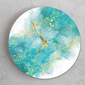 Può includere: Un orologio rotondo color turchese e oro su sfondo bianco. Il quadrante dell'orologio ha un design simile all'acquerello con accenti di glitter dorati.