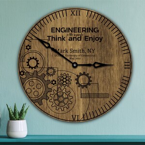 May include: A wooden clock with a brown background and black gears. The clock face has the text "ENGINEERING is like a puzzle Think and Enjoy" and "Mark Smith, NY UCONN, University of Connecticut May, 2023".