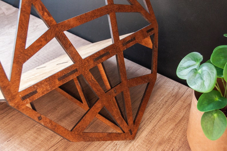 May include: A geometric wooden shelf with a brown wood finish. The shelf is made of multiple pieces of wood that are joined together to create a geometric pattern. The shelf is sitting on a wooden surface.