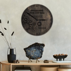 May include: A wooden clock with a black background and white gears and text. The clock face reads "Engineering of the Mind Think and Enjoy" and includes the name "Mark Smith, NY" and the date "May 2023".