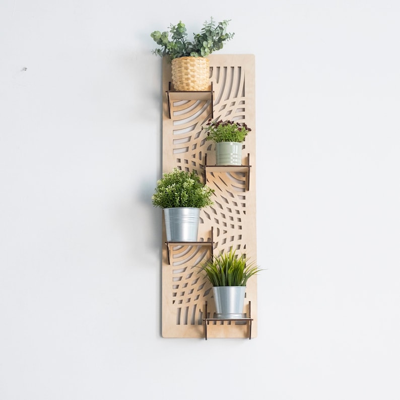 May include: A wooden wall-mounted planter with a geometric design. It has four shelves to hold potted plants. The planter is made of light brown wood and has a natural finish.