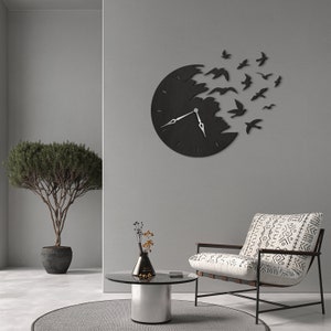 May include: A black wall clock with a unique design, featuring a clock face that appears to be breaking apart, with birds flying out. The clock has silver hands and is mounted on a gray wall. The overall theme is modern home decor.