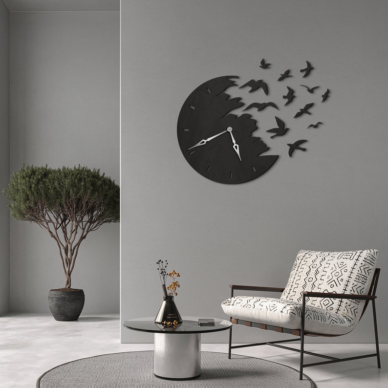 May include: A black wall clock with a unique design, featuring a clock face that appears to be breaking apart, with birds flying out. The clock has silver hands and is mounted on a gray wall. The overall theme is modern home decor.
