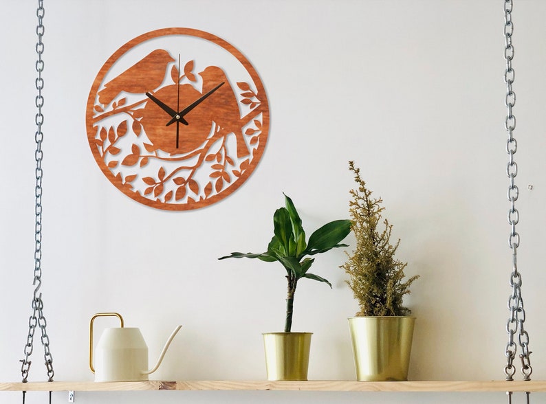 May include: A wooden wall clock with a brown finish features a silhouette of two birds perched on a branch with leaves. The clock face is visible with black hands and a white background.