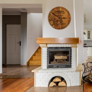 May include: A wooden clock with a brown background and black gears and hands. The clock face reads "Engineering Think and Enjoy" with the text "Mark Smith, NY" below. The clock is hanging on a white wall above a white brick fireplace.