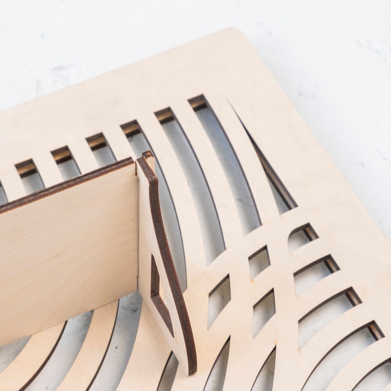 May include: A wooden shelf unit with a geometric design. The shelf is made of light brown wood and has a series of cutouts in the shape of circles and squares.