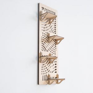 May include: A wooden wall shelf with a geometric pattern and four shelves. The shelves are made of light wood and have a simple design.