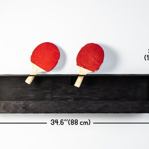 May include: Black wooden wall shelf with two red ping pong paddles. The shelf is 34.6 inches wide and 7.9 inches tall. The paddles are 3.9 inches in diameter.