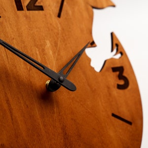 May include: A wooden clock face with black hands and a white silhouette of a bird. The clock face is brown and has the numbers 12 and 3 visible.