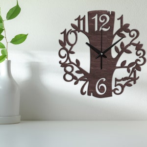 May include: A brown wooden wall clock shaped like a tree with black hands and black numbers around the edge. The clock is hanging on a white wall.