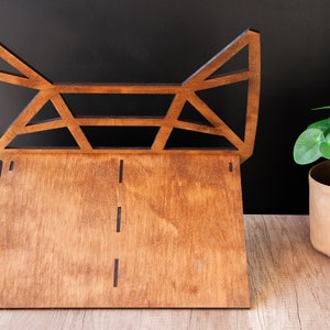 May include: A wooden geometric shelf with a triangular design. The shelf is made of dark brown wood and has a natural finish. The shelf is standing on a light brown wooden surface.