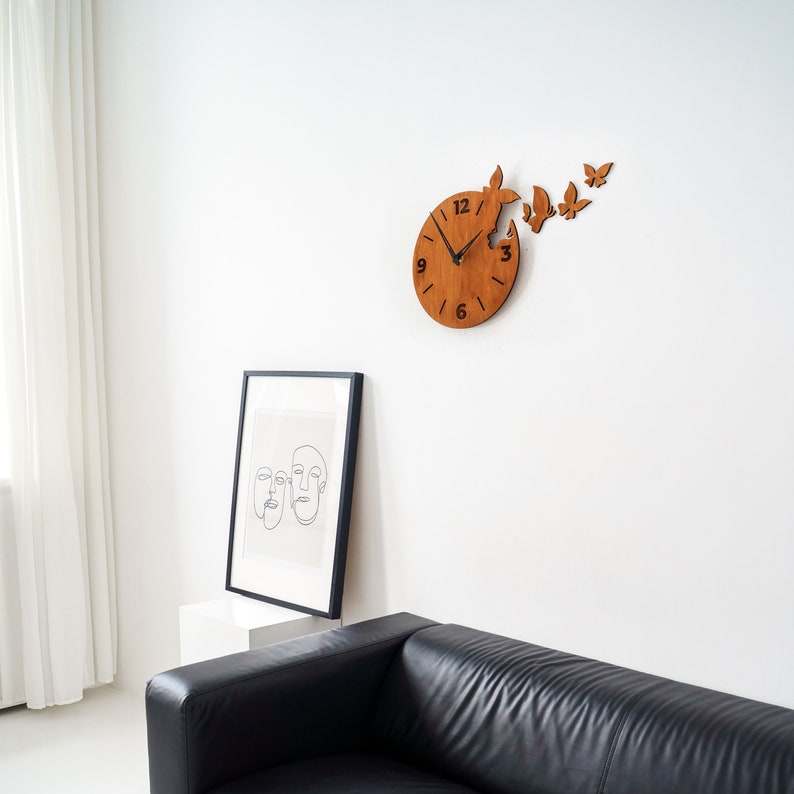 May include: A wooden clock with a butterfly design. The clock is mounted on a white wall and has black hands and numbers. The clock is surrounded by several smaller butterfly cutouts.