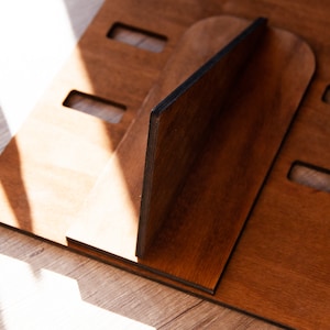 Puede incluir: Un soporte de madera para port&aacute;til en un tono marr&oacute;n c&aacute;lido. El soporte est&aacute; construido con m&uacute;ltiples piezas de madera, con ranuras y una pieza de soporte central. El dise&ntilde;o sugiere un enfoque en la funcionalidad y la est&eacute;tica minimalista.