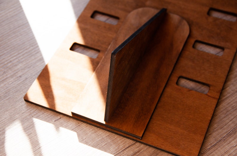 Puede incluir: Un soporte de madera para port&aacute;til en un tono marr&oacute;n c&aacute;lido. El soporte est&aacute; construido con m&uacute;ltiples piezas de madera, con ranuras y una pieza de soporte central. El dise&ntilde;o sugiere un enfoque en la funcionalidad y la est&eacute;tica minimalista.