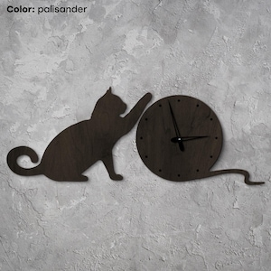 Könnte beinhalten: Eine Wanduhr aus dunklem Holz, die eine Katze zeigt, die nach einem runden Zifferblatt greift. Die Uhr hat schwarze Zeiger und den Text "Color: palisander". Das Design ist für die Wandmontage vorgesehen.