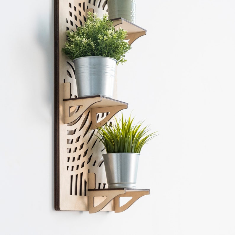 May include: A wooden wall shelf with three tiers, each with a metal plant pot. The top shelf has a green plant, the middle shelf is empty, and the bottom shelf has a green grass-like plant.