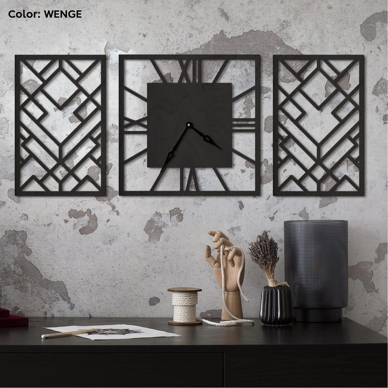 Może przedstawiać: Trzyczęściowy zestaw zegara ściennego z czarnym wykończeniem. Centralny zegar ma rzymskie cyfry i wskaz&oacute;wki. Dwa geometryczne panele flankują zegar. Kolor to WENGE. Zegar jest zamontowany na teksturowanej szarej ścianie.