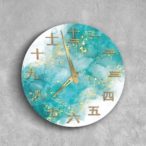 May include: A round teal and white clock with gold accents and gold numbers. The clock face has a watercolor-like design with gold glitter.