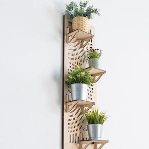 May include: A wooden wall-mounted shelf with a geometric design, featuring four shelves holding potted plants. The shelves are made of light brown wood and the plants are in various sizes and types.