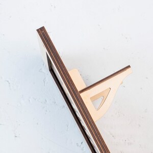 May include: A wooden shelf unit with a dark brown frame and light wood shelves. The shelf unit has a unique design with a triangular support brace on the bottom shelf.
