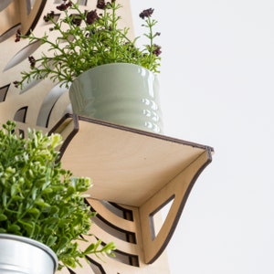 May include: A wooden wall shelf with a light brown finish. The shelf has a curved design and is made of plywood. A small green ceramic planter with a green plant is sitting on the shelf.