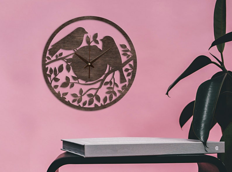 May include: A brown wooden clock with a silhouette of two birds perched on a branch with leaves. The clock has a simple design with black hands and a white face.