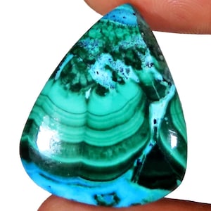 May include: A polished, teardrop-shaped gemstone with a vibrant display of colors. The stone features swirling patterns of deep teal, turquoise, and dark green, with accents of light blue. The gem is held between two fingers, showcasing its natural beauty.