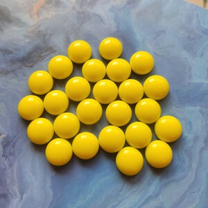 Peut inclure: Une collection de 20 perles de verre jaune vif, disposées en cercle sur un fond bleu.