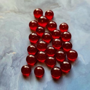 May include: A group of 20 red glass beads, scattered on a blue and white marbled surface.