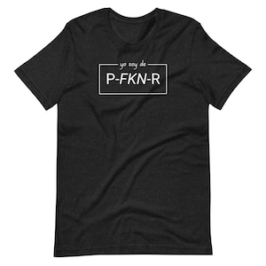 May include: Dark gray t-shirt with the text "yo soy de P-FKN-R" in a white rectangular box. The text is in a handwritten style. The shirt is made of a soft material and has short sleeves.