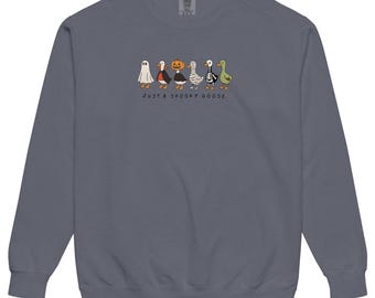 May include: A slate blue sweatshirt featuring a whimsical illustration of five cartoon geese dressed in Halloween costumes. The text "JUST A SPOOKY GOOSE" is printed below the geese in a playful font. The sweatshirt has a crew neck and long sleeves.