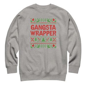 Puede incluir: Una sudadera gris con un diseño de punto rojo y verde. El diseño incluye las palabras "GANSTA WRAPPER" en rojo, junto con árboles de Navidad, corazones y renos. La sudadera tiene cuello redondo y mangas largas.