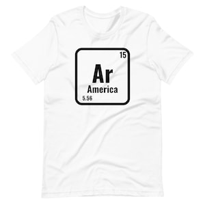 May include: White t-shirt with a black square graphic. The graphic features the letters "Ar" above the word "America" and the number "5.56". The number "15" is in the top right corner of the square.