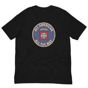 Op de afbeelding: Zwart T-shirt met een distressed cirkelvormige afbeelding. De afbeelding luidt "ALL AMERICAN AIRBORNE ALL THE WAY" in een cirkelvormig ontwerp met een rood en blauw embleem in het midden. Het shirt is gemaakt van een zacht materiaal.