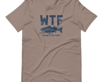 May include: A tan t-shirt with the text "WTF" above a blue fish illustration. Below the fish, the text reads "WHERE'S THE FISH?" The shirt has a crew neck and short sleeves.