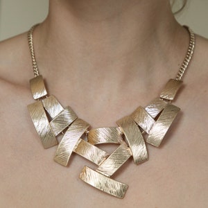 May include: A gold-toned statement necklace with a geometric design. The necklace is made of multiple interlocking pieces that create a modern and edgy look.