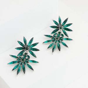 May include: A pair of silver earrings with two green crystal flower designs. The larger flower has a smaller flower design in the center.