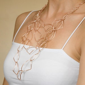 Peut inclure: Un collier en or rose avec un design superposé de formes géométriques entrelacées. Le collier est fait de fil métallique et a un aspect délicat et féminin.