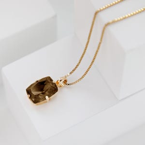 Op de afbeelding: Een gouden ketting met een bruine edelsteen hanger. De hanger is rechthoekig met gefacetteerde randen.